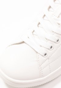 Fehér sneaker sima bőr felsőrésszel, lapos fehér fűzőkkel, hat fémlyukkal és textúrált gumitalppal, finom varrott díszítésekkel.