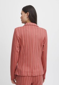 Rose-colored blazer with vertical white stripes, tailored fit, notched collar, and smooth fabric texture. Features slim, long sleeves.