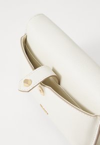Hvit teksturert skinnlommebok med gullknappåpning, åpen klaff og synlig innvendig fôr på hvit bakgrunn.