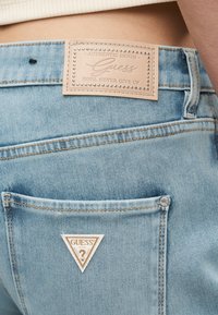 Ανοιχτό μπλε τζιν παντελόνι με πίσω τσέπη που διαθέτει έμπλαστρο λογότυπο Guess και ένα δερμάτινο ετικέτα ραμμένη στη μέση της ζώνης.