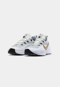 Pair of white and gray athletic sneakers with black soles, black eyelets, white laces, and a large gold Nike swoosh on the side, on a white background.