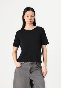 T-shirt noire à manches courtes avec un col rond, fabriqué en matériau doux. Associé à un jean gris à jambes larges, avec une texture légèrement délavée.
