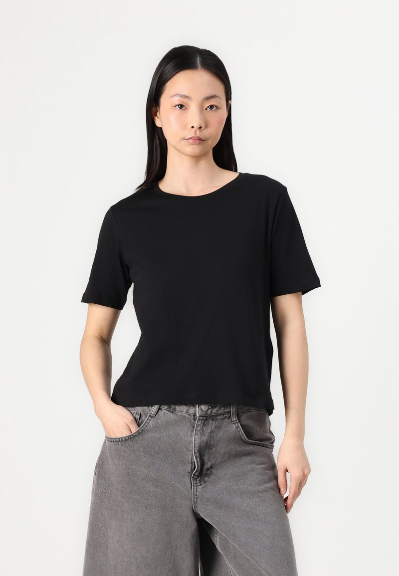 T-shirt noire à manches courtes avec un col rond, fabriqué en matériau doux. Associé à un jean gris à jambes larges, avec une texture légèrement délavée.