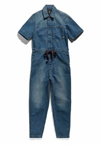 Combinaison en denim bleu foncé avec des manches courtes, fermeture éclair à l'avant, poche poitrine, deux poches latérales et un détail de taille nouée. Légère décoloration sur le tissu.