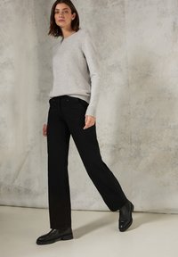 Grijze geribde trui, zwarte wijd-uitlopende broek en zwarte enkellaarsjes. De outfit heeft een eenvoudig ontwerp met een neutraal kleurenpalet.