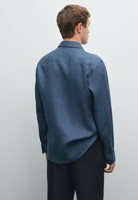 Navy blue button-up shirt made of soft fabric with a smooth texture, long sleeves, and rounded hem. Paired with pinstriped trousers.