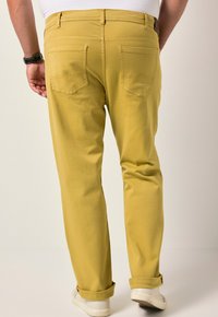 Žluté bavlněné kalhoty s rovnými nohavicemi. Mají dvě zadní kapsy s zakřiveným švem. Dokončeny ohrnutými manžetami a bílými teniskami.