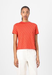 Red patterned t-shirt with a round neckline, short sleeves, and a slightly cropped fit. The fabric has a smooth, soft texture.