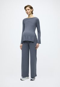 Γκρι ριμπ χιτώνιο εγκυμοσύνης που αποτελείται από μπλούζα με μακριά μανίκια και πλαϊνές σχισμές και παντελόνι με φαρδιά πόδια, συνδυασμένο με ανοιχτό γκρι αθλητικά παπούτσια.