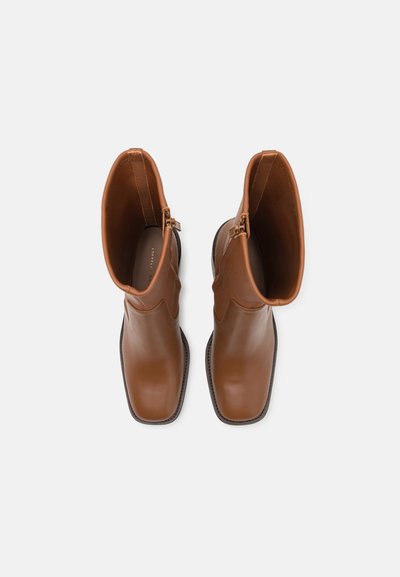 Bottes en cuir marron jusqu'à la cheville avec une finition lisse, bout pointu et fermeture éclair sur le côté. Présente un design légèrement festonné le long du tige.