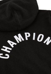 Felpa nera con cappuccio caratterizzata da testo "CHAMPION" ricamato in bianco disposto a semicerchio sul retro. Il tessuto presenta una finitura morbida e texturizzata.