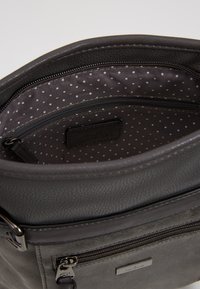Sac à main en cuir gris avec une finition texturée. L'intérieur doublé présente un motif à pois. Inclut un compartiment zippé et une quincaillerie estampillée.