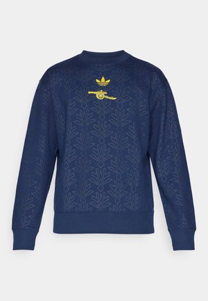 Granatowy sweter z delikatnym wzorem, okrągłym dekoltem i ściągaczami na rękawach. Zawiera żółte logo z pociskiem oraz charakterystycznymi pasami.