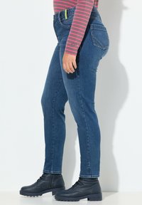 Mörkblå denimjeans med smal passform, som visar framfickor och ett lätt avsmalnande ben; kombinerat med svarta snörstövlar.