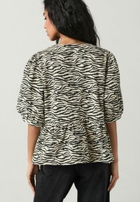 Peplum bluse i cremefarvet og sort zebra mønster, med korte pufærmer, en gatherings talje og en blød tekstur.