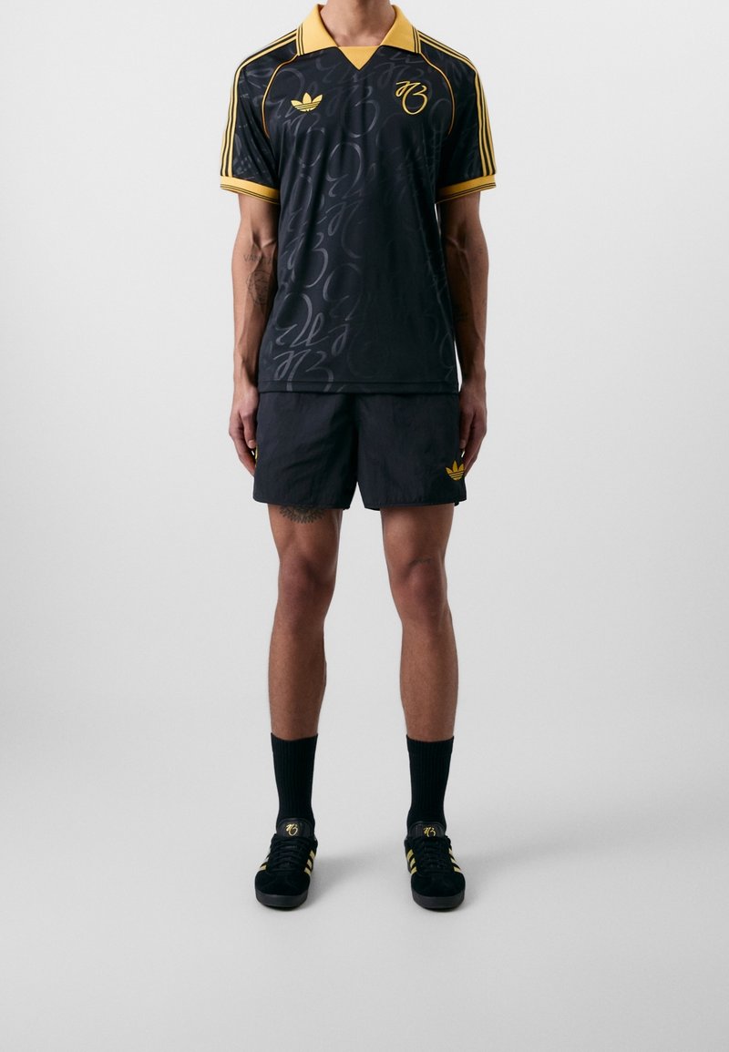 Maillot noir avec des accents jaunes, présentant un motif subtil et un design col, associé à un short noir assorti et des chaussures.