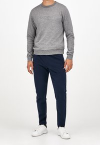 Sudadera gris con logotipo en relieve, combinada con pantalones azul marino y zapatillas blancas. Diseño simple, cuello redondo y puños acanalados.