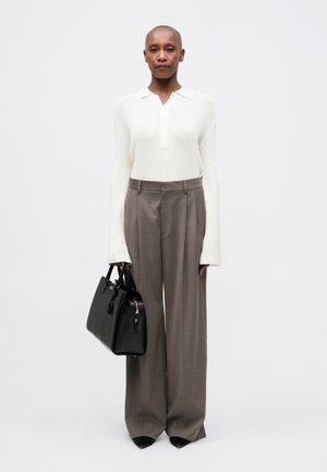 Top bianco a maniche lunghe con costine e colletto, abbinato a pantaloni beige larghi a vita alta. Borsa nera con due manici.