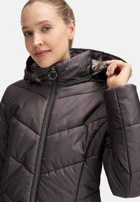 Gequiltede donkergrijze pufferjas met een hoge kraag, rits aan de voorkant en bontvoering, met een diagonaal stikpatroon en verstelbare koorden.