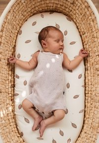 Een licht lila gebreide babyromper met knoopaccenten, liggend op een gevoerde ondergrond versierd met bruine bladpatronen, in een geweven mand.