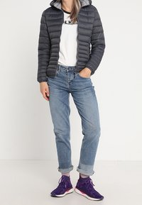 Chaqueta acolchada gris con capucha sobre una camiseta blanca, combinada con vaqueros azules remangados y zapatillas deportivas moradas con detalles rosas.