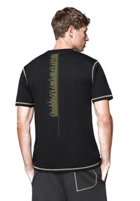 Czarna koszulka z pionowym wzorem żółtego tekstu z tyłu. Kontrastowe przeszycia wzdłuż rękawów i dolnego obszycia dodają detali.