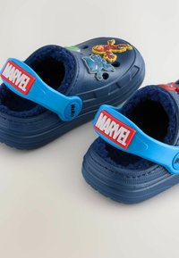 Sabots en caoutchouc bleu avec un doublure douce bleu marine, présentant des accents de personnages Marvel et des sangles bleues ajustables avec le logo rouge "MARVEL".