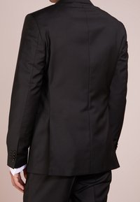 Svart skräddarsydd kavaj med en strukturerad design, slät textur, enkel vent bak och knappade ärmslut. Minimal detaljering.