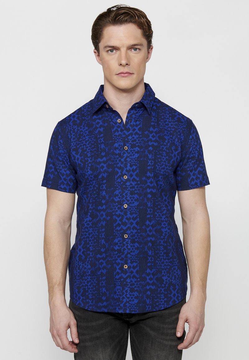 Camicia a maniche corte con bottoni, caratterizzata da un motivo blu su sfondo blu scuro, con colletto a punta e bottoni in legno.