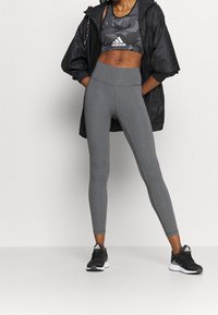 Leggings grises de tela elástica, combinados con una chaqueta negra corta y un sujetador deportivo de patrón camuflaje. Unos zapatos deportivos negros completan el look.