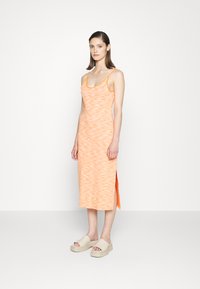 Vestido maxi laranja trançado com decote em forma de U e fendas laterais, combinado com sandálias platform bege claro. Textura suave, design casual.