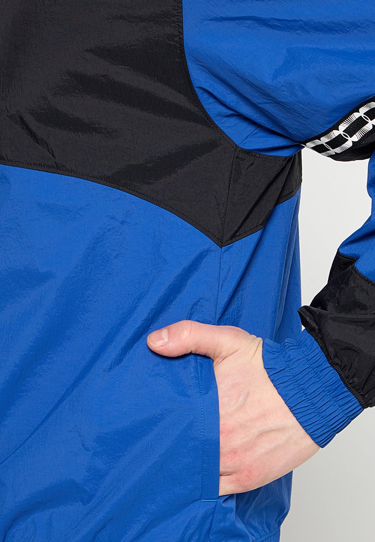 Chaqueta azul y negra con textura acolchada, puños elásticos, un bolsillo lateral y detalles con patrones a lo largo de la manga.