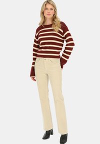 Sweter w paski w kolorze burgunda i kremowym z szerokimi rękawami, w połączeniu z jasnymi spodniami z sztruksu i czarnymi botkami za kostkę.