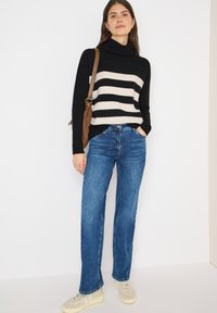 Pull à col roulé rayé noir et crème, jeans droits bleus et baskets beiges, avec un sac en bandoulière marron. Textures de tissus lisses visibles.