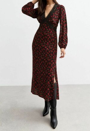 Vestido negro con estampado floral, mangas largas abullonadas y detalles de encaje; presenta un escote en V profundo y aberturas laterales. Combinado con botas negras hasta la rodilla.