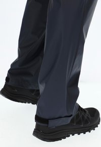 Marine waterdichte broek met een gladde textuur, gecombineerd met zwarte sportieve schoenen met een robuuste zool en klittenbandaccenten.