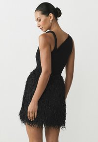 Black dress featuring a fitted bodice with a one-shoulder design and a short, textured skirt made of fringed fabric.