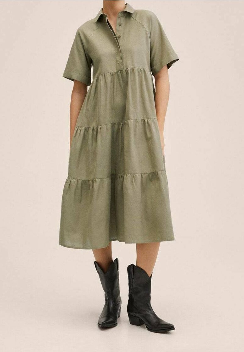 Olivgrünes, knielanges Kleid mit kurzen Ärmeln, Knopfleiste und gestuftem Rockdesign, kombiniert mit schwarzen Cowboy-Stiefeln.