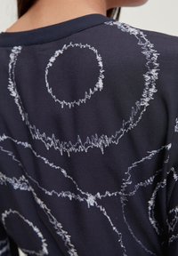Top in tessuto navy con un motivo astratto bianco unico caratterizzato da linee circolari e ondulate; texture liscia e design a vestibilità rilassata.