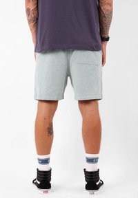 Shorts en velours côtelé vert clair avec une poche arrière, associés à des baskets montantes noires et des chaussettes blanches avec un accent bleu.