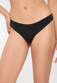 Slips da bikini neri con una superficie liscia, design a vita bassa e copertura minima, caratterizzati da un bordo pulito senza motivi o accessori.
