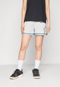 Lyse grå atletiske shorts med blå kant, der har en sidelomme og en afslappet pasform. Bæres med sorte sneakers og hvide ankelstrømper.