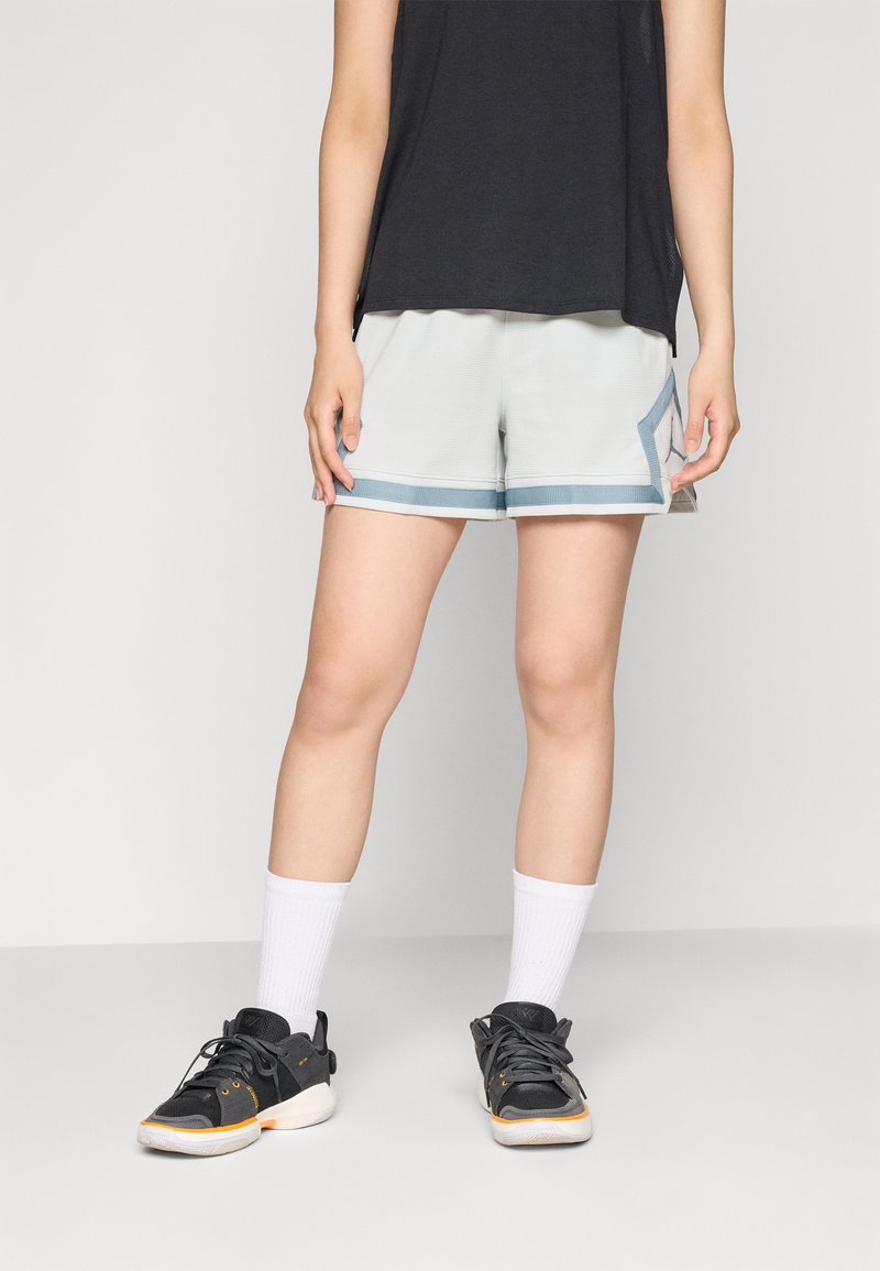 Lyse grå atletiske shorts med blå kant, der har en sidelomme og en afslappet pasform. Bæres med sorte sneakers og hvide ankelstrømper.
