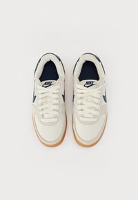 Nike-sneakers met een crèmekleurige canvas bovenwerk, marineblauwe accenten en een gumrubberen zool. Bevat witte veters en een geweven logo op de tong.