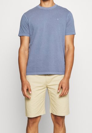 Kurzärmliges, blaues Baumwoll-T-Shirt mit rundem Halsausschnitt, kombiniert mit beigen Shorts. Verfügt über ein kleines Logo auf der Brust.