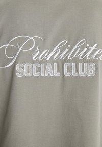 Tricou din bumbac de culoare verde măsliniu, cu text brodat "Interzis" în cursiv și "SOCIAL CLUB" în font de tip bloc, ambele în alb.