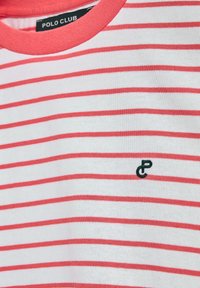 Vit bomull T-shirt med tunna horisontella röda ränder. Har en rund korallfärgad midja och en liten svart logotyp på bröstet.