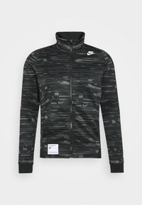 Svart zip-up jacka med hög krage, med en texturerad mönster och Nike-logotyp. Inkluderar en vit etikett vid fållen.