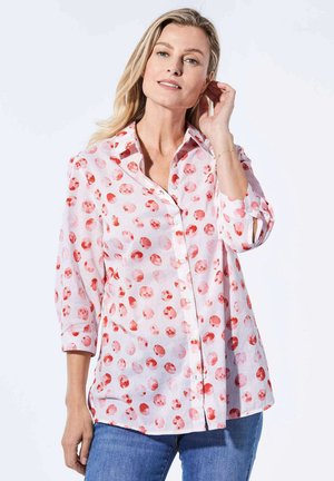 Chemise en lin légère avec un fond rose et un motif à pois rouges. Elle possède un col et de longues manches avec des poignets retroussés.