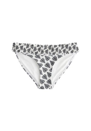 Frau in weißem Bikini mit schwarzen Blattmustern, von hinten gesehen, stehend in der Nähe von hellfarbenem Stoff und klarem Himmel im Hintergrund.